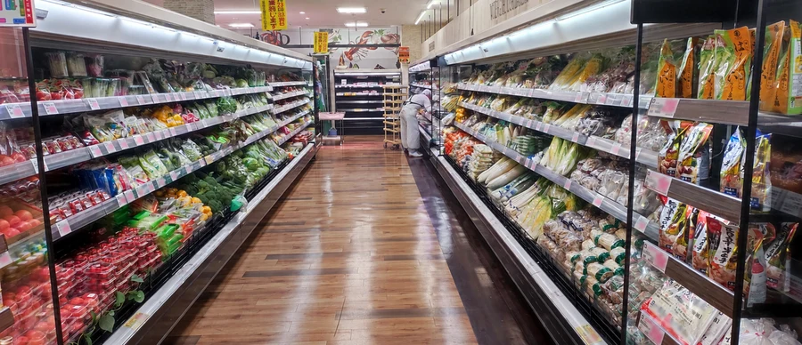 青木店の農産売場通路に並ぶトマトや大根等の新鮮な野菜棚