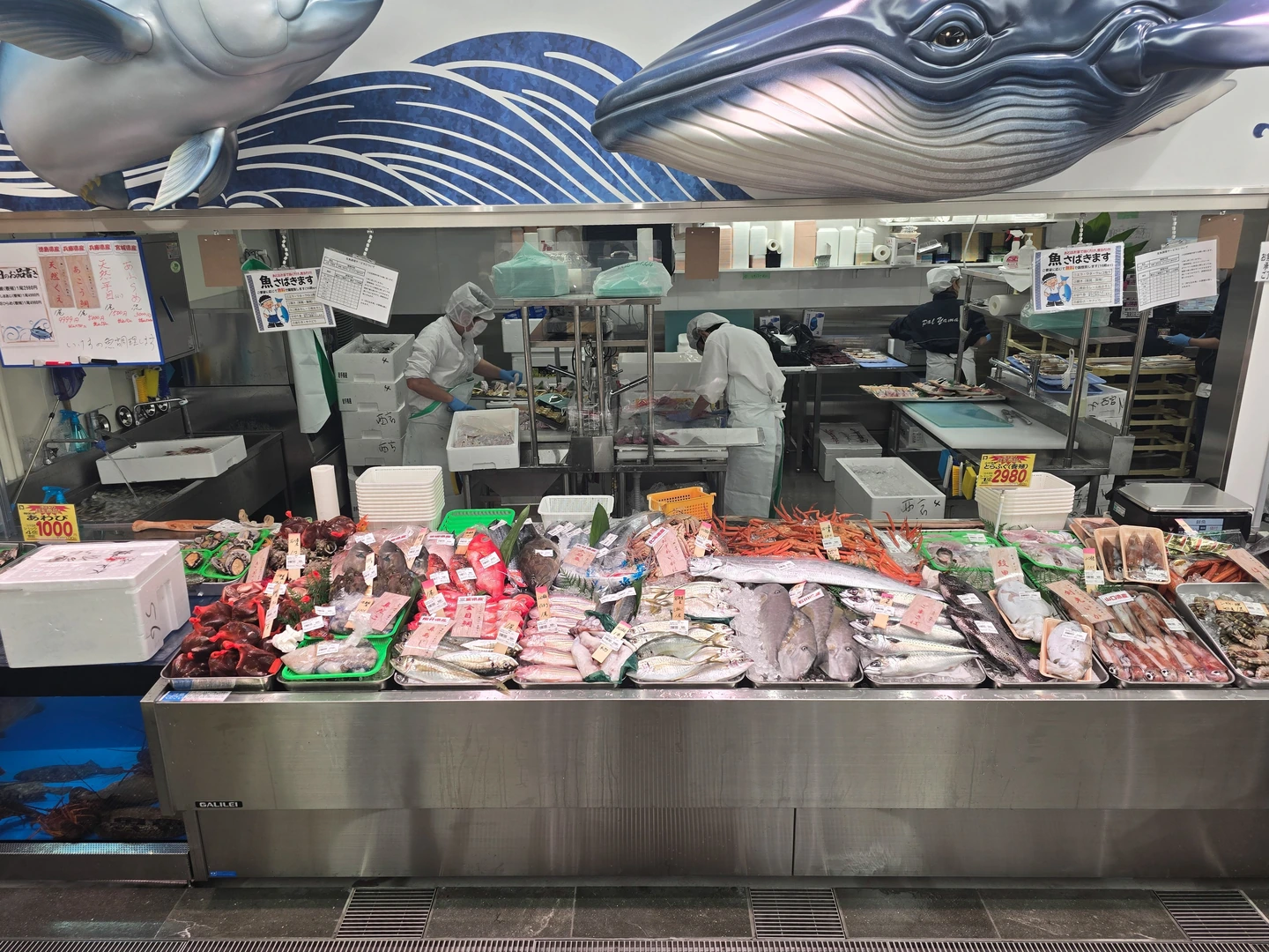 西宮店の対面水産売場。魚が並ぶケースの奥に、マスクと帽子を着用した担当者がいます。